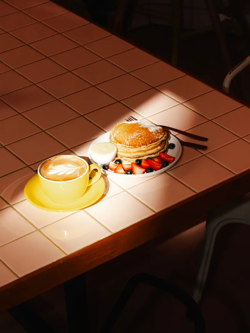 Panquecas e café ao sol na mesa de azulejo rosa